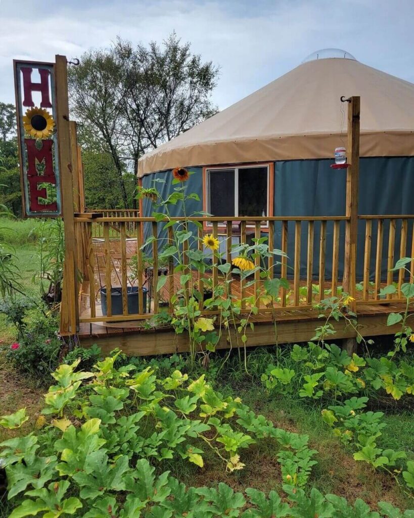 A yurt in a field with sunflowers in the foreground
